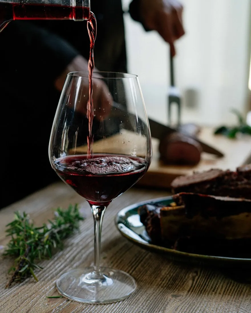 Red wine being poured into a glass at a set table
